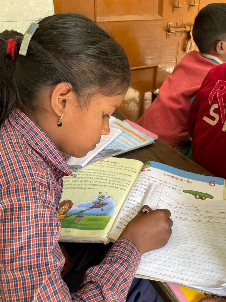 A young student writing in her notebook- Lakshya Trust Lakshya Paathshaala